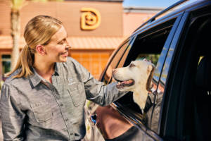 A Dogtopia employee petting a dog through the car window out front of a Dogtopia location