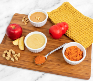 Food board with apple, pumpkin, and other condiments in bowls, with red KONG toy